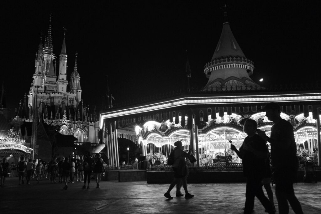 people walking in front of moving carousel with the Disney Castle in the background at night.